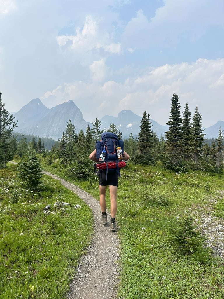 Hiker with backpack running on mountain trail surrounded by pine trees and mountains in background