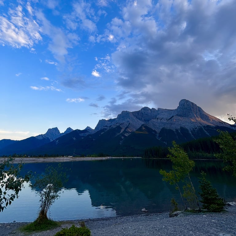 Mountain lake landscape with snow-capped peaks reflected in calm turquoise water under a blue sky with clouds