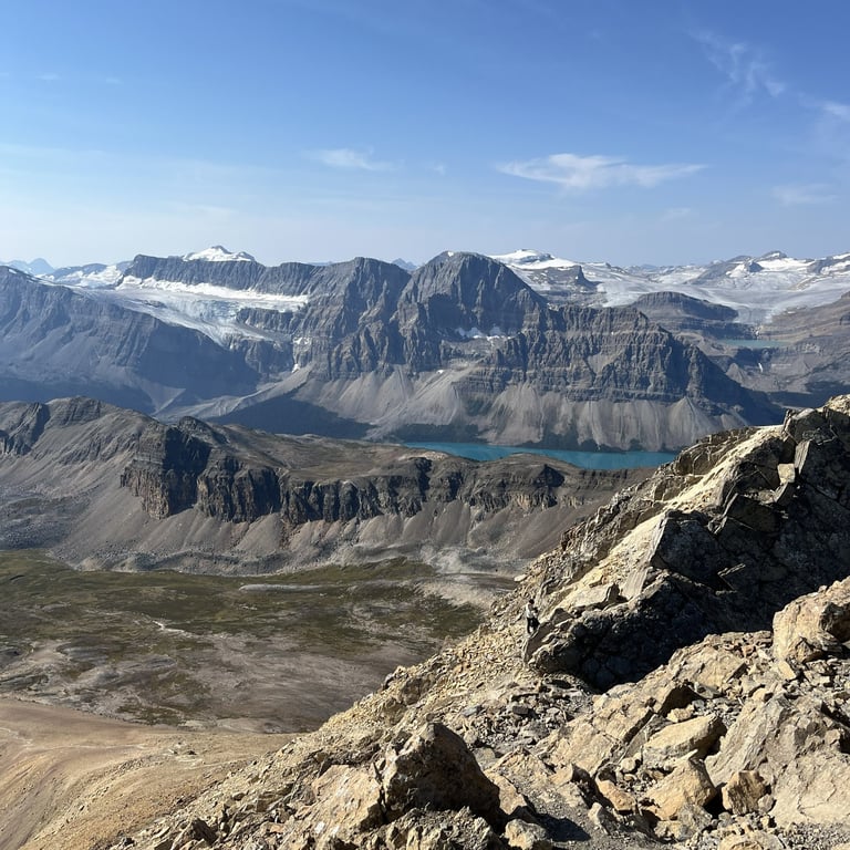 Alpine landscape with jagged mountain peaks, turquoise glacial lake, rocky terrain, and clear blue sky